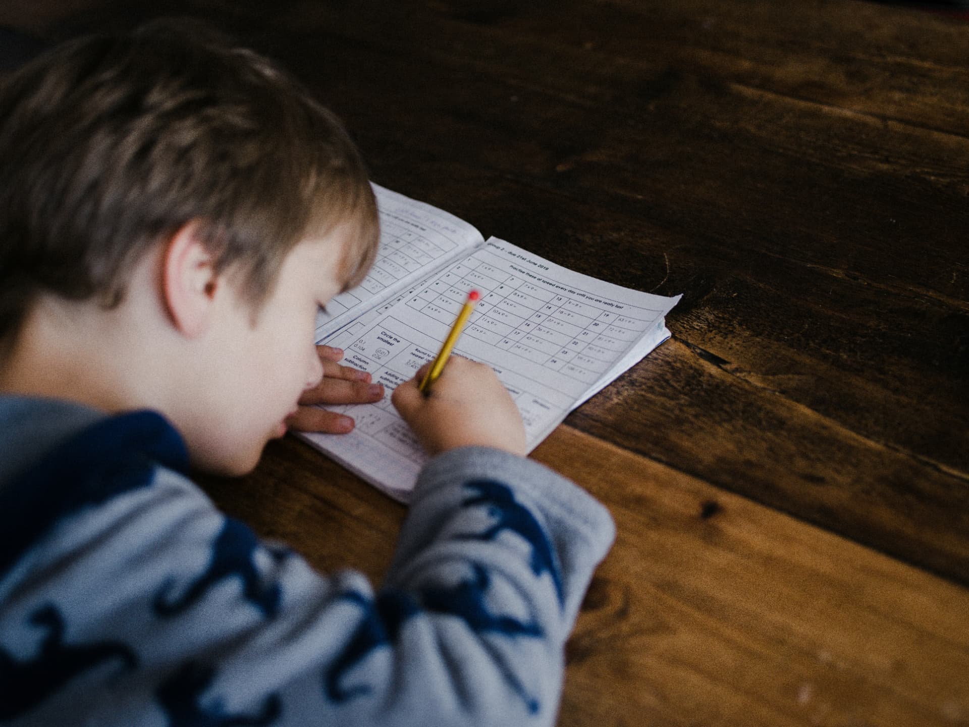 A young student concentrating on a maths worksheet with a pencil in hand