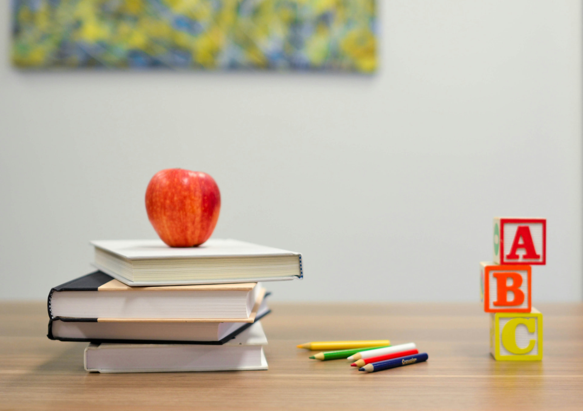 A stack of books, an apple and alphabet blocks on a primary classroom desk